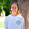 Young woman with brunette hair and blonde highlights smiles for her photo wearing a white shirt. Photo captured by Jaden Mezetin Photography.
