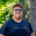 Young man wears glasses and an Eastern T-shirt outside, smiling for his picture. Photo captured by Jaden Mezetin Photography.