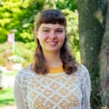 Young woman with brunette hair smiles for her photo wearing a white and yellow shirt. Photo captured by Jaden Mezetin Photography.